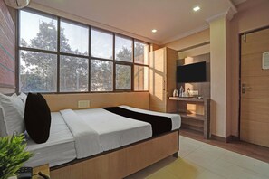 Quarto de hotel com cama, televisão, escrivaninha e janela com vista para árvores.