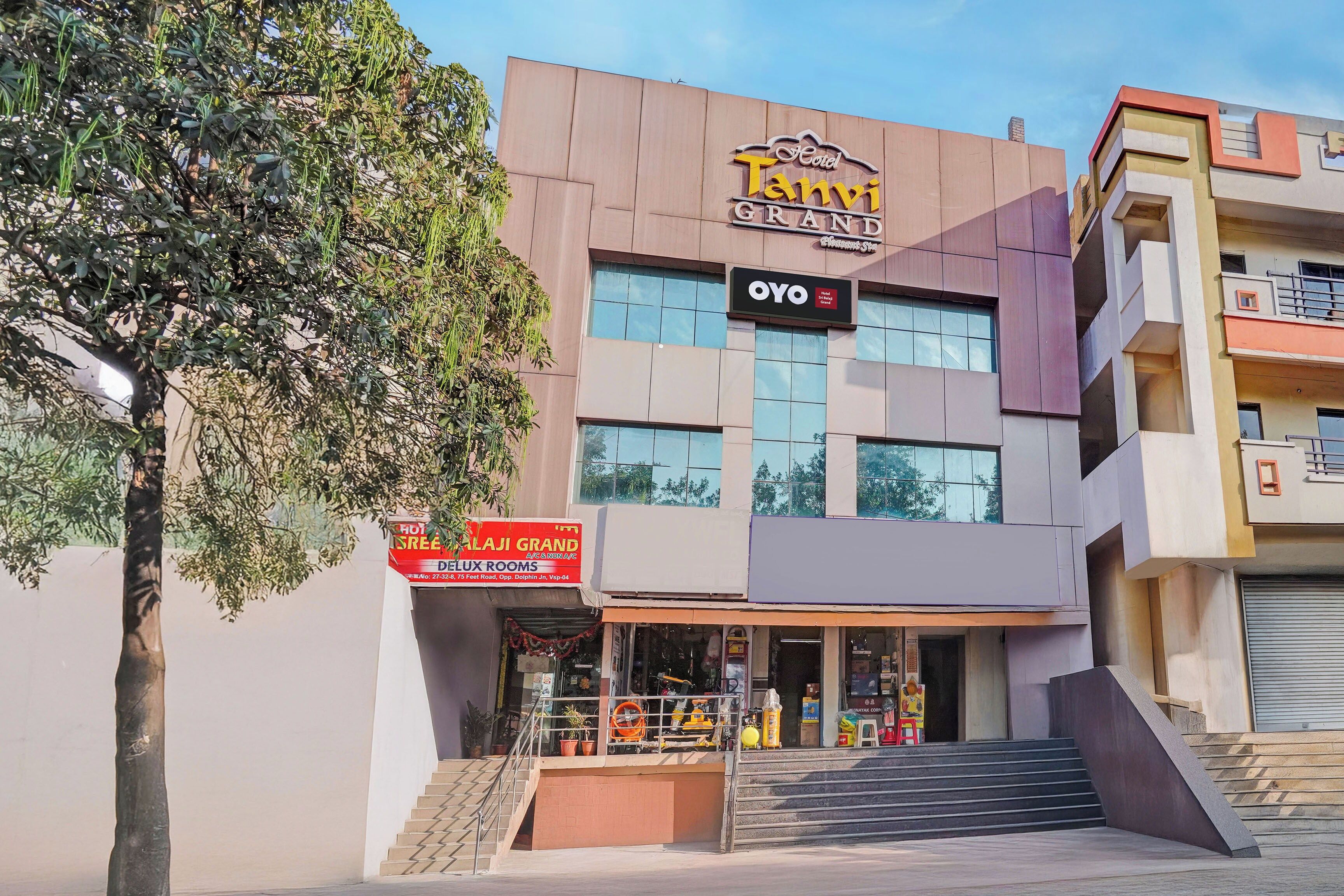 A hotel named 'TANVI GRAND' with a sign for 'OYO Hotel' and a storefront for 'DELUXE ROOMS'.