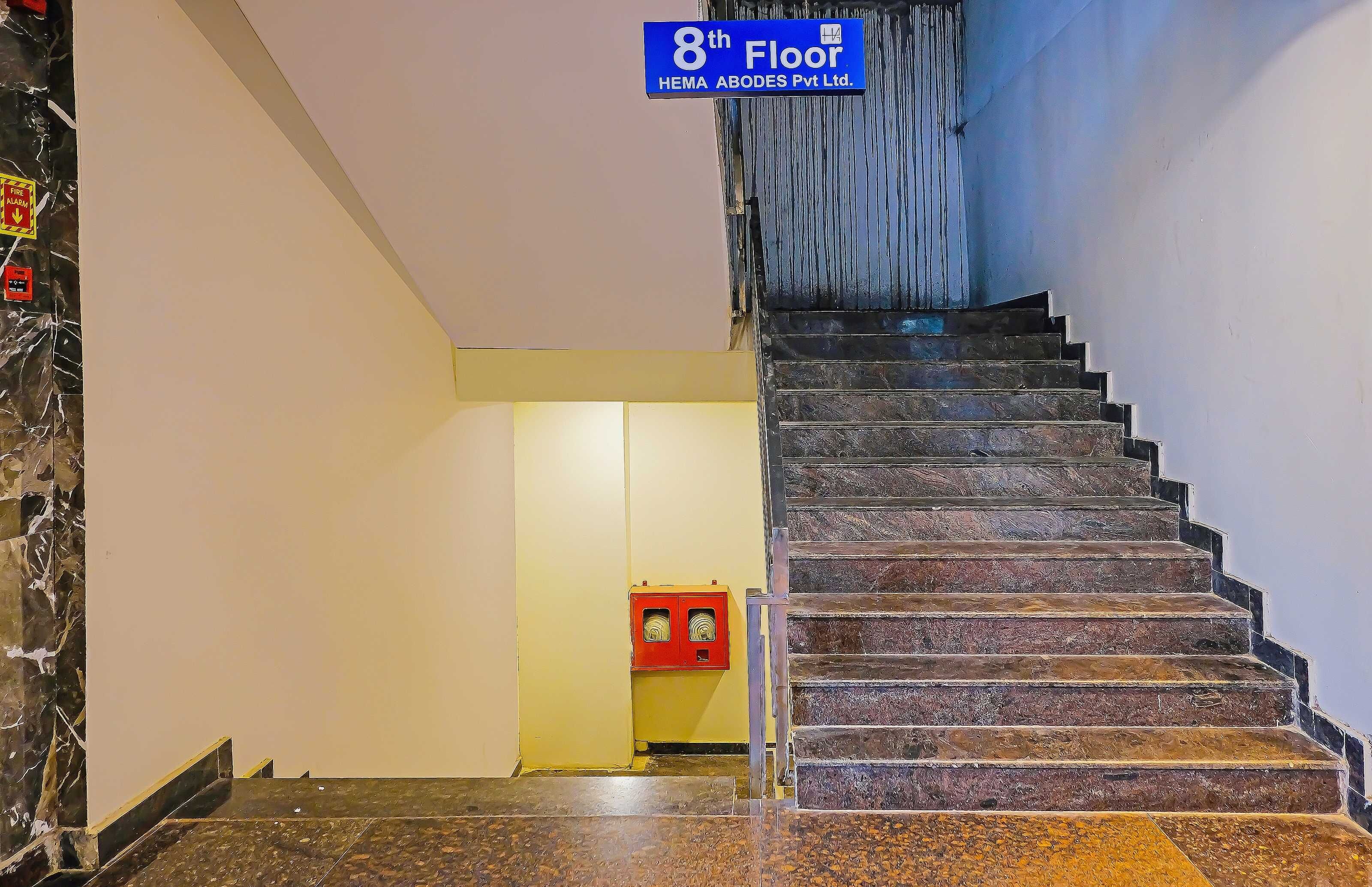 Un escalier menant au 8e étage, avec une alarme incendie et une boîte rouge d’urgence fixée au mur.