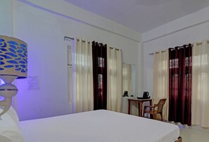 A hotel room with a bed, a table with a chair, a lamp, and curtains. - HOTEL O SURYA INN (Varanasi)
