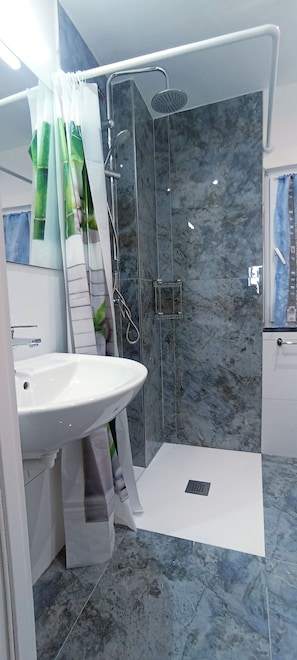 A bathroom with a white sink, a shower with a glass door, and a marble floor. - Appartamento Venere in Villa Daria (Chiavari)