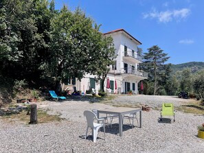 A two-story building with a balcony, surrounded by trees and a gravel area with outdoor furniture. - Appartamento Venere in Villa Daria (Chiavari)