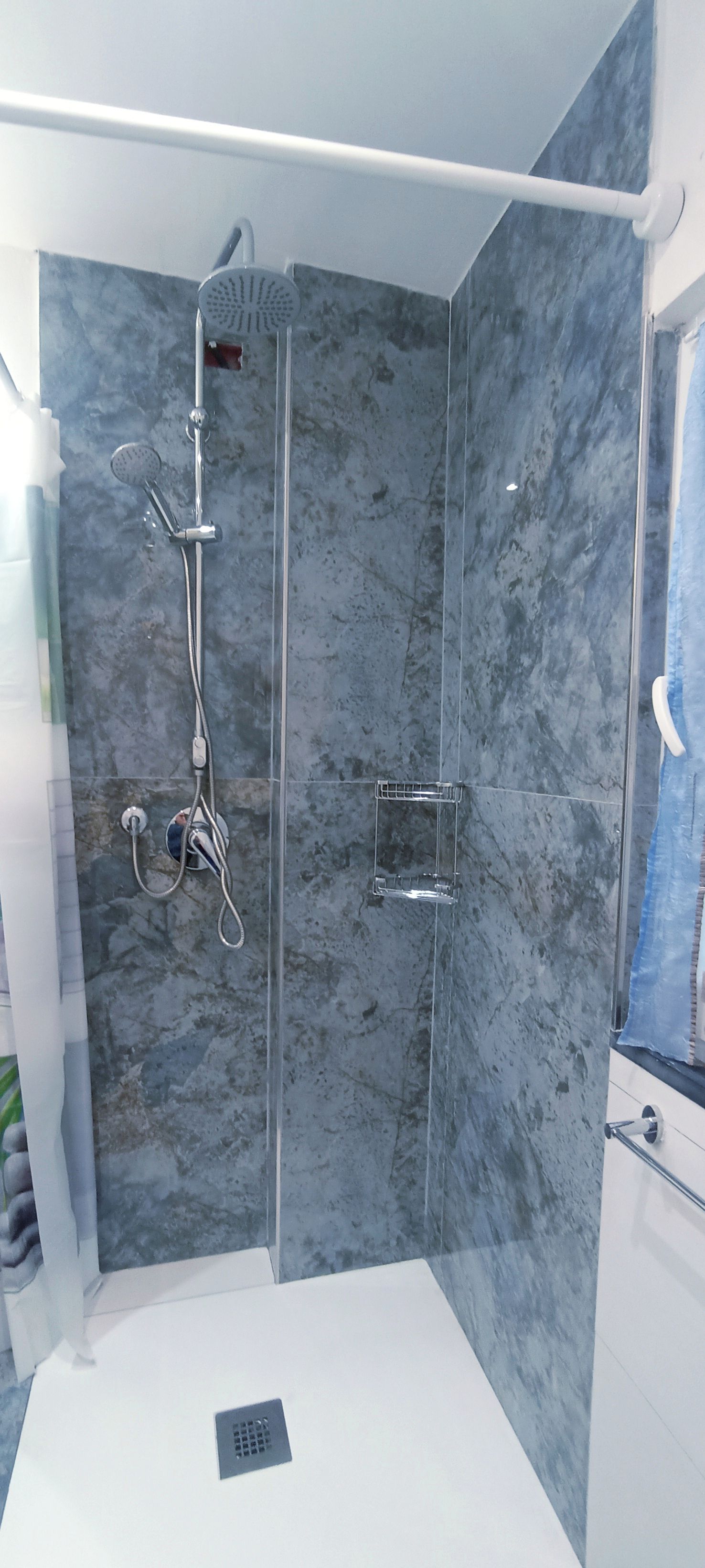 A modern bathroom with a shower, marble walls, and a white sink.