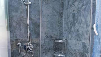 A modern bathroom with a shower, marble walls, and a white sink.