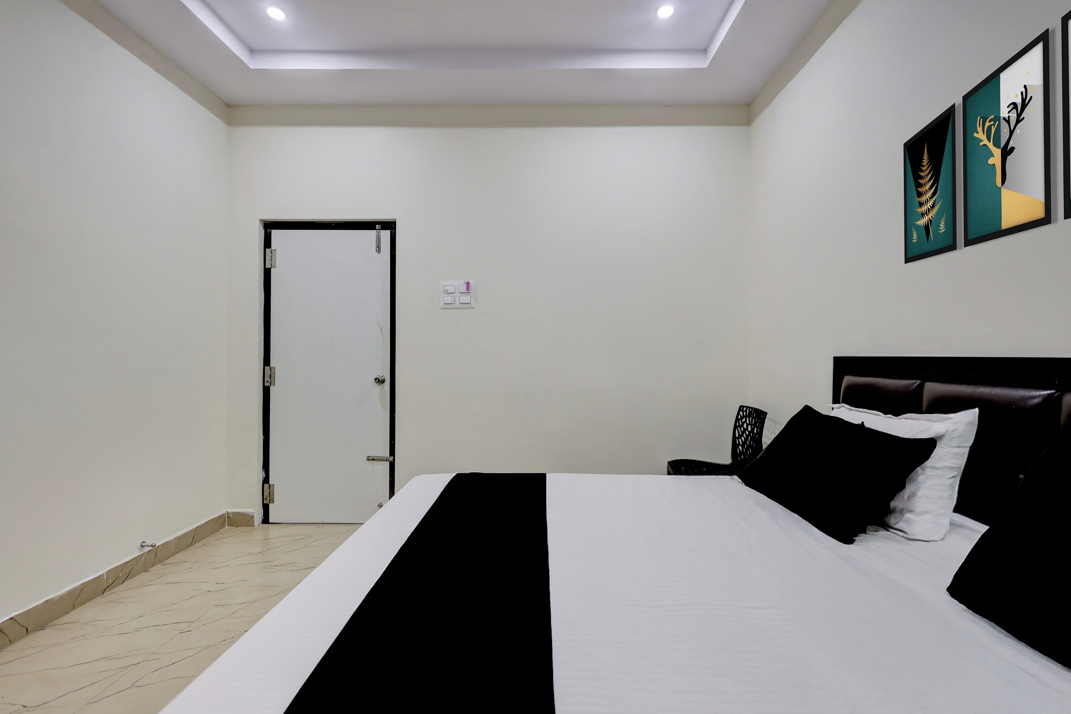A hotel room with a bed, a nightstand, a door, and wall-mounted artwork.