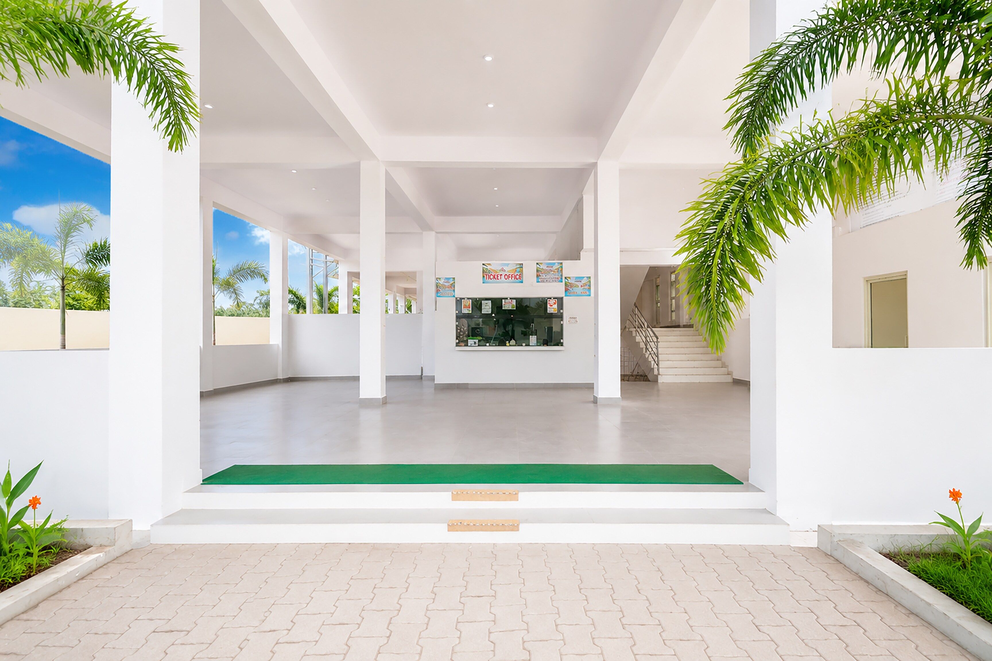A spacious indoor area with a ticket office, a staircase, and a green carpet leading to a door.