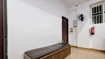 A hallway with a bench, a door, a wall-mounted fan, a fire extinguisher, and a window with bars.