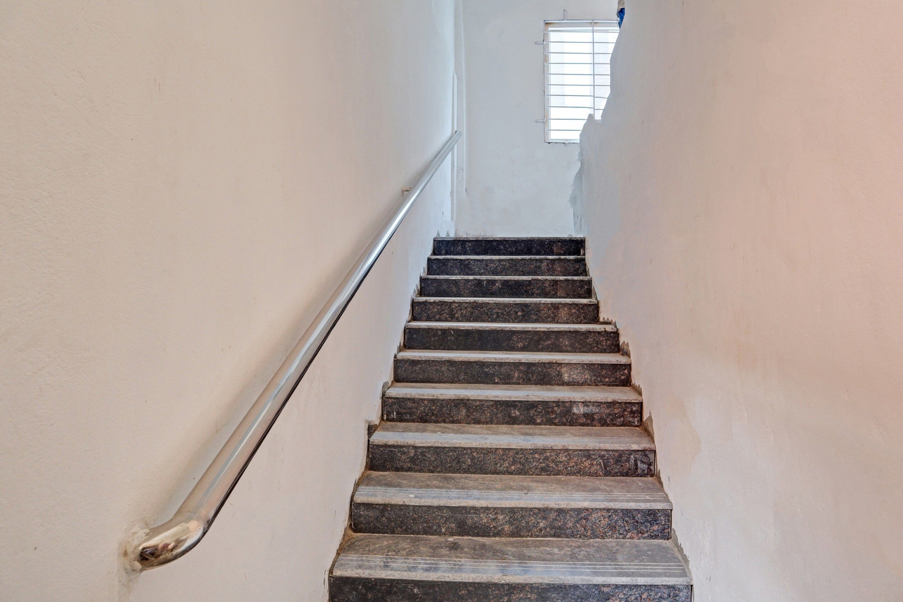 A staircase with a metal handrail leading up to a window.