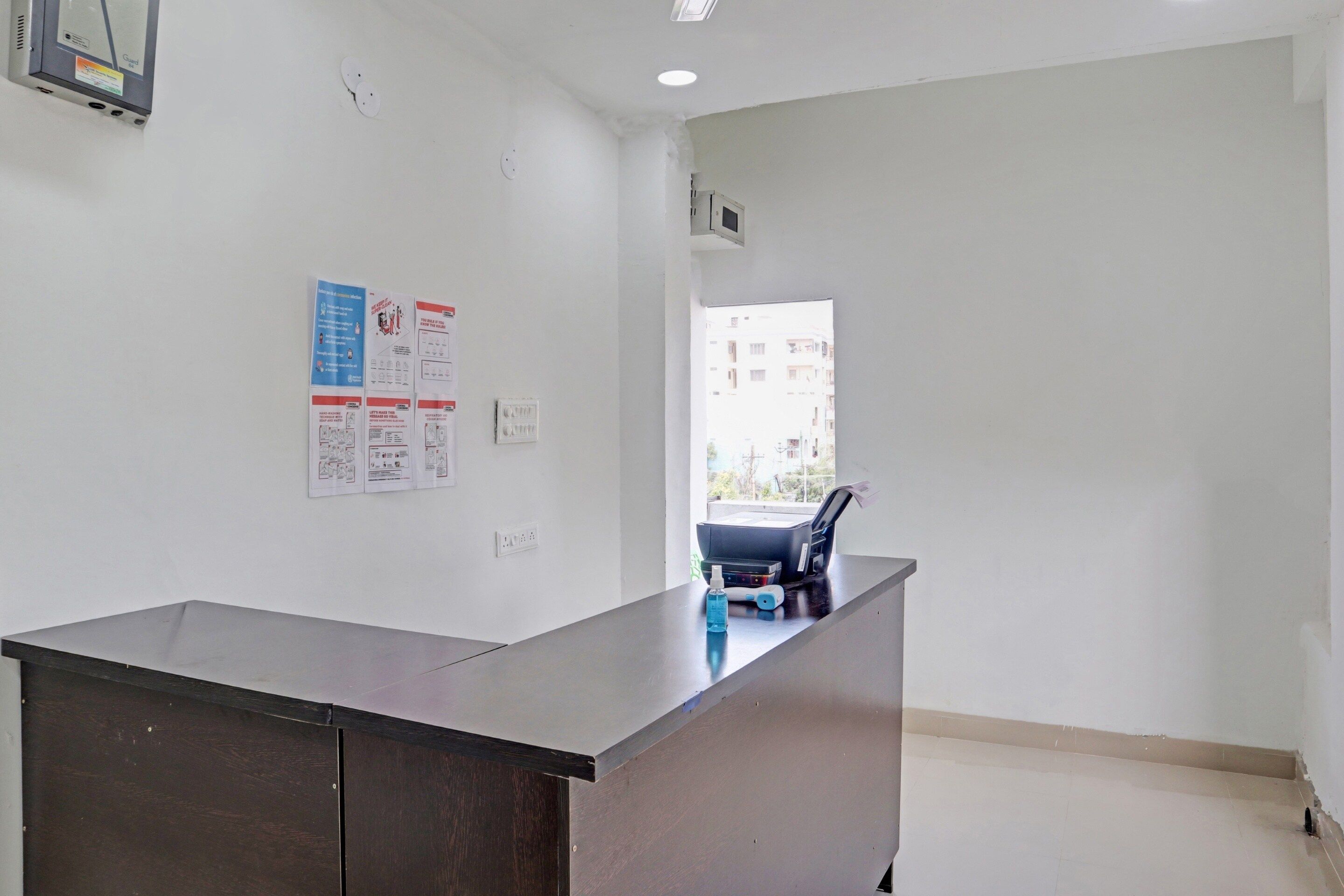 A reception desk in a hotel lobby with a window view, a wall-mounted intercom, and a few informational posters.