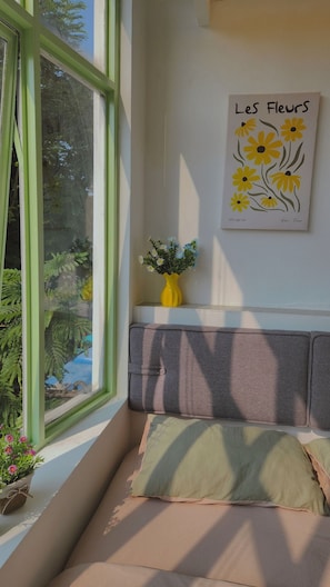A room with a window, a painting titled 'Les fleurs,' a yellow vase with flowers, and a cushioned bench. - D1 Heart · Parkside & Rooftop · Leafy @ Cozinema (Ben Thanh, District 1)