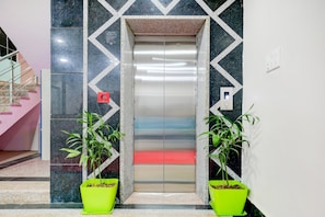 An elevator with a geometric wall design, two potted plants, and a staircase to the left. - Hotel O Navneeta Grand (Varanasi)