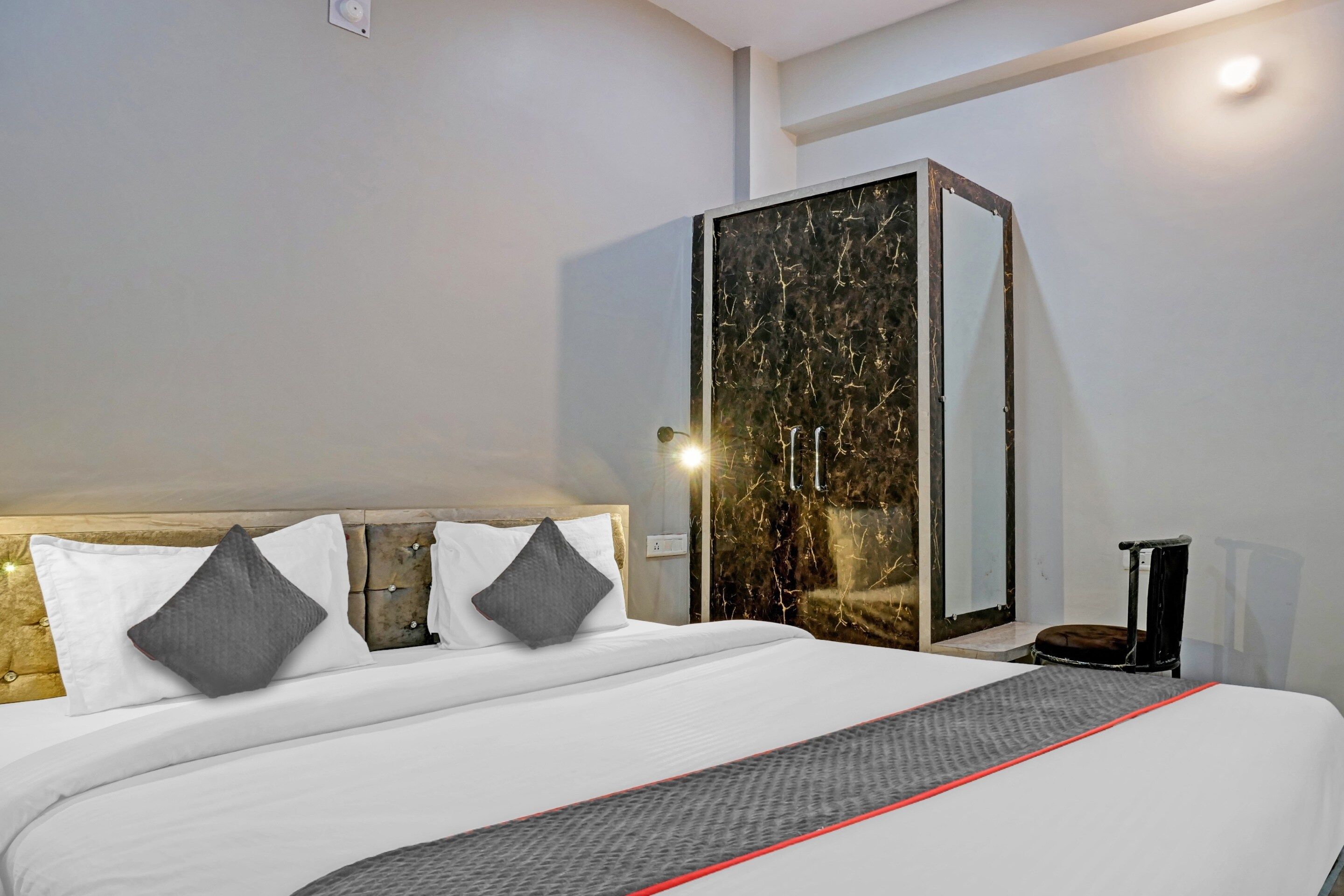 A modern hotel room with a large bed, a wardrobe with a marble-like finish, and a bedside table with a lamp.