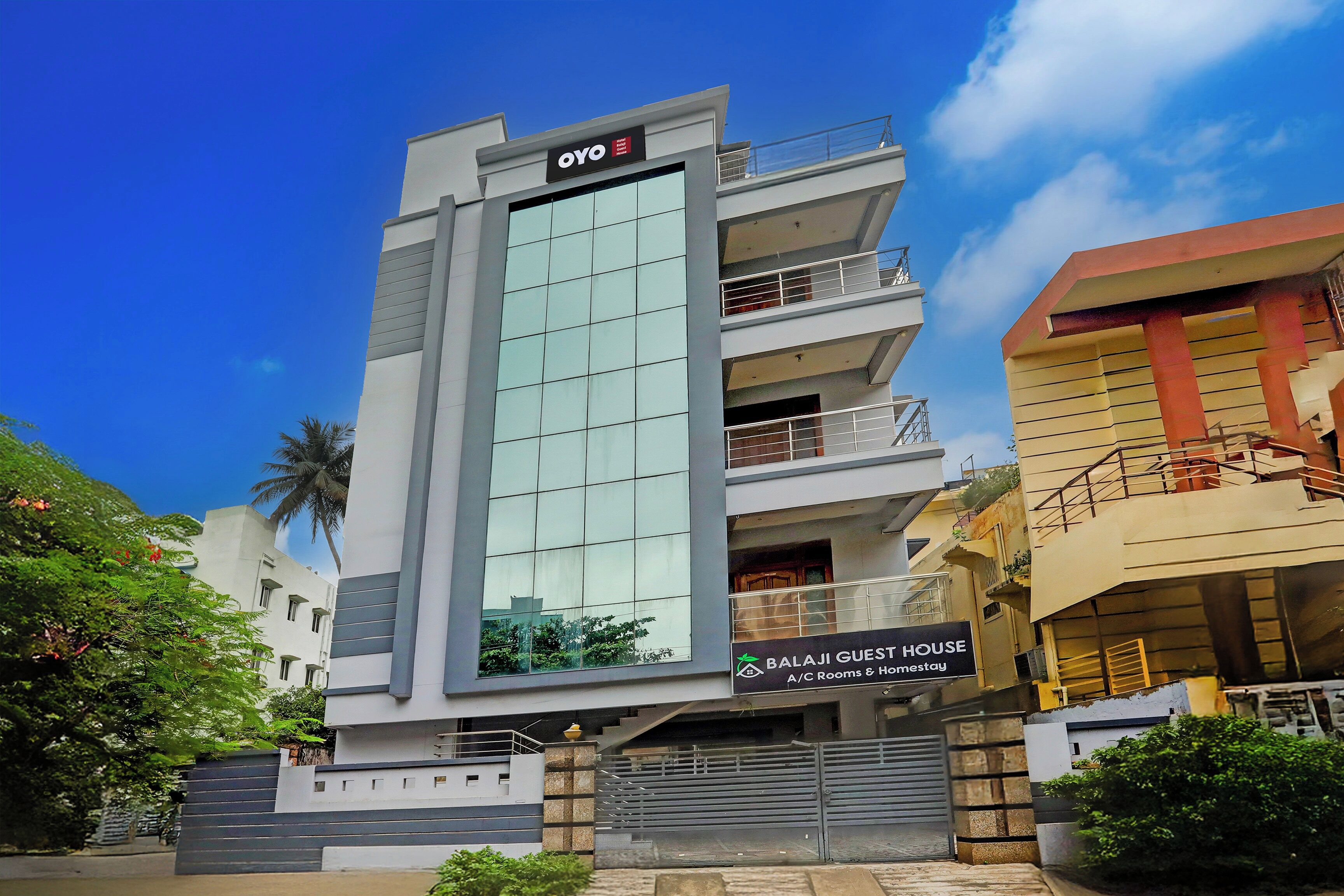 A multi-story building with a prominent OYO logo on the facade, a Balaji Guest House sign, and a gated entrance.