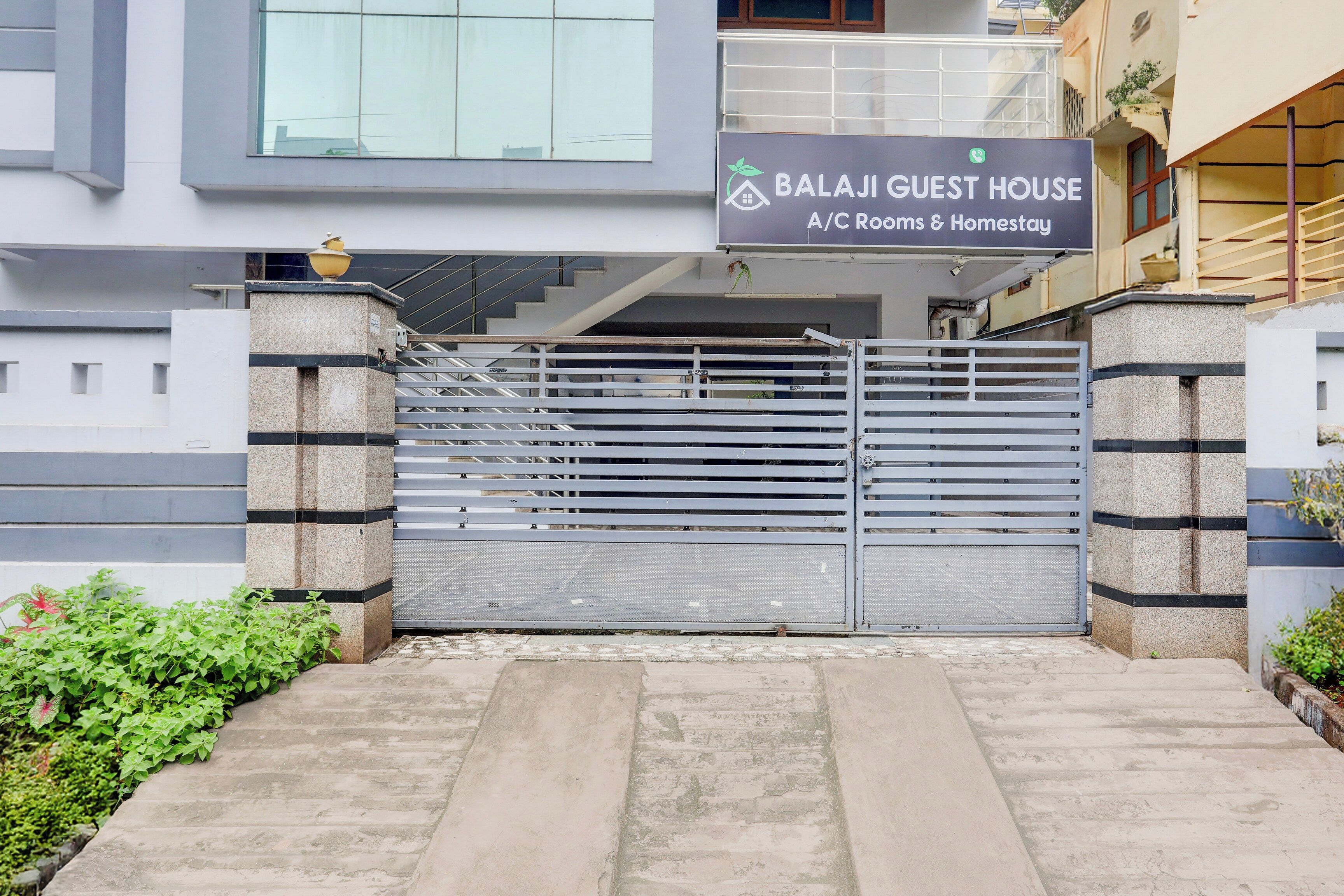 A gated entrance to a property named 'BalaJi Guest House' with a modern architectural design, featuring a metal gate and a staircase leading to the entrance.
