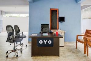 Un salón de conferencias con un escritorio etiquetado 'OYO', dos sillas de oficina, una silla de madera, un televisor en la pared y una ventana con vistas.