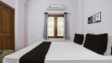 A hotel room with a bed, a window with curtains, an air conditioning unit, and a wall-mounted artwork.