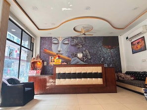 Uma área de recepção com um grande mural na parede, um ventilador de teto e um espaço de estar com sofás e poltronas.