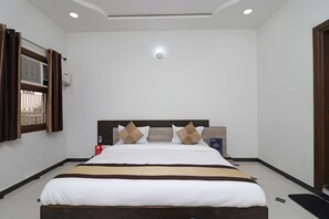 Quarto de hotel com uma cama grande, cabeceira com telefone, mesa de cabeceira com um cartão e janela com cortinas.