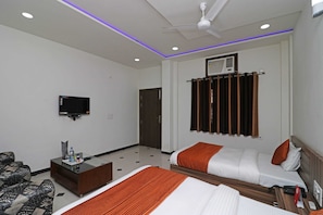 Habitación de hotel con dos camas, televisión, escritorio y ventilador de techo.