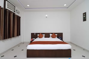 Quarto de hotel com uma cama grande, mesa de cabeceira, ar condicionado fixado na parede e luminária no teto.