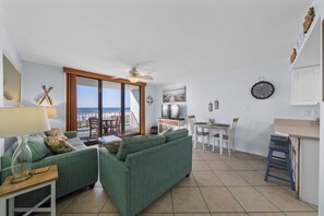 Una sala de estar moderna con un sofá verde, un comedor y vistas al mar a través de amplios ventanales.