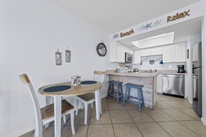 Une cuisine moderne avec des meubles blancs, un îlot central doté de tabourets, un four encastré et une horloge au mur.