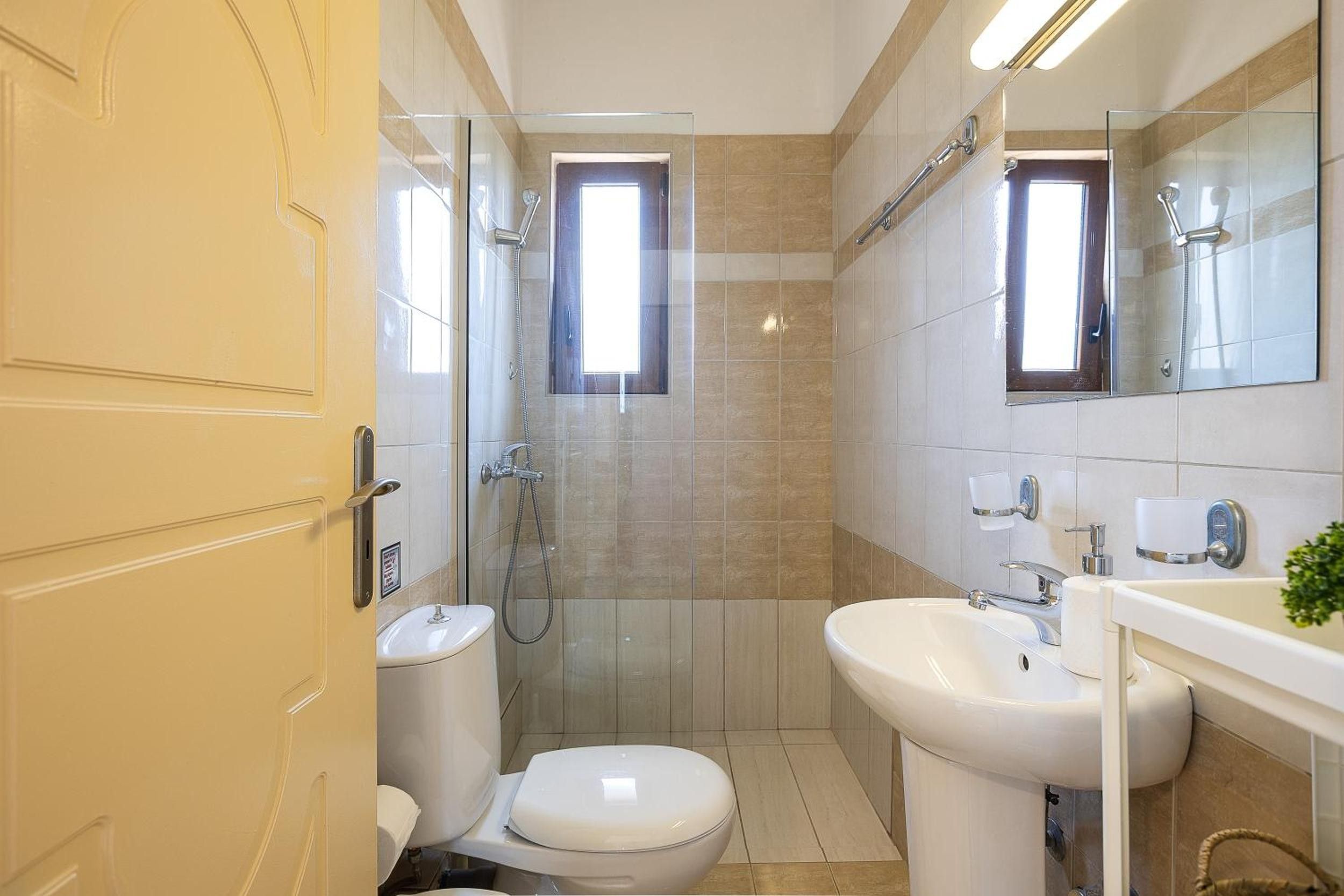 A bathroom with a toilet, sink, shower, and a mirror.