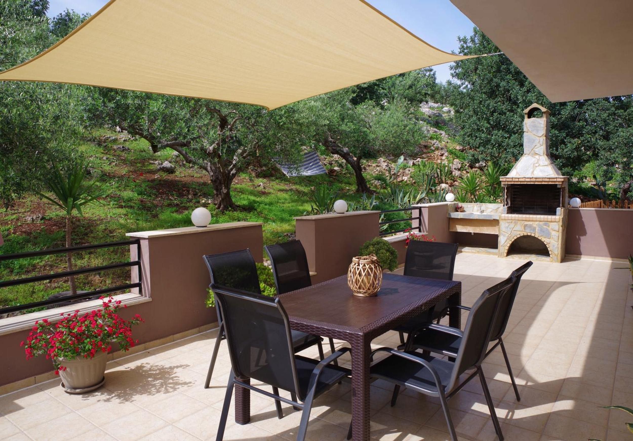 An outdoor patio with a table and chairs, a barbecue grill, and a view of trees and landscape.