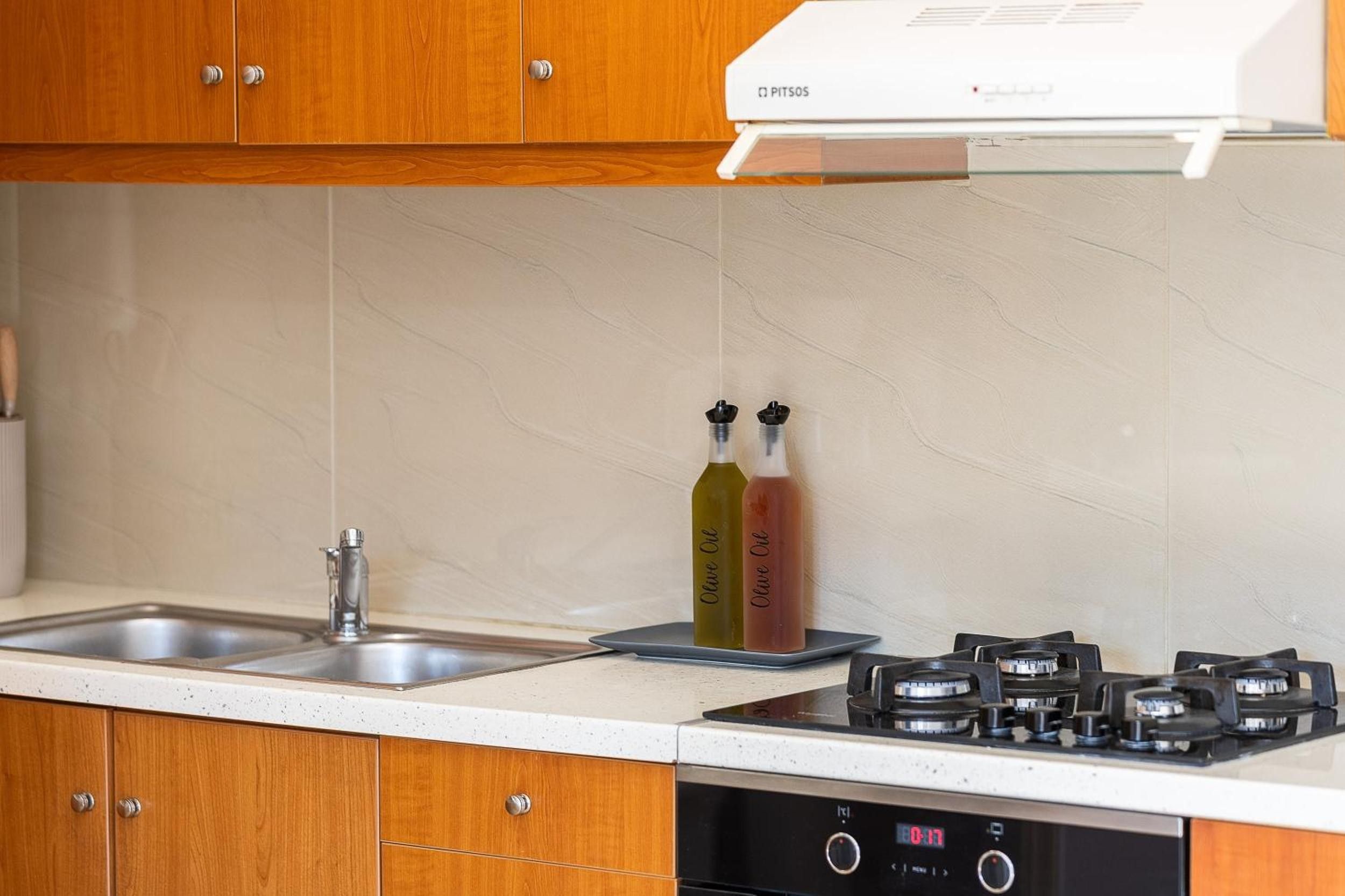 A kitchen with wooden cabinets, a stainless steel sink, a gas stove, and two bottles of olive oil.
