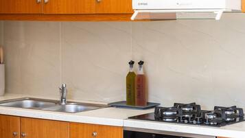 A kitchen with wooden cabinets, a stainless steel sink, a gas stove, and two bottles of olive oil.