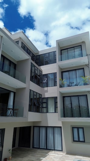A multi-story building with balconies, large windows, and a courtyard with potted plants. - Lovely 2-bedroom apartment with lift, swimming pool in Grand Baie (Grand Baie)
