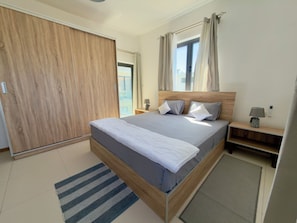 A modern bedroom with a large bed, wooden wardrobe, bedside tables, and a view of the outdoors. - Lovely 2-bedroom apartment with lift, swimming pool in Grand Baie (Grand Baie)