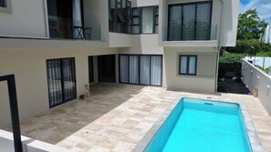 A modern two-story building with a swimming pool, large windows, and a tiled patio area. - Lovely 2-bedroom apartment with lift, swimming pool in Grand Baie (Grand Baie)