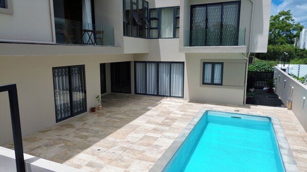 Un edificio moderno de dos pisos con piscina, ventanas amplias y un patio con baldosas.