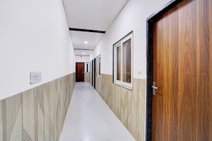 A hallway with a tiled floor, wooden doors, and a plain wall with a light switch. - Hotel O Brijbhav Vrindavan The Spiritual (Vrindavan)