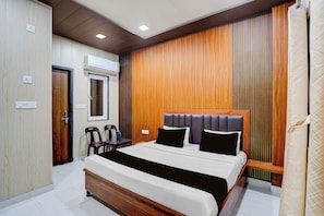 A bedroom with a bed, a wooden headboard, a desk with chairs, and an air conditioning unit. - Hotel O Brijbhav Vrindavan The Spiritual (Vrindavan)