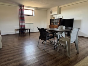 A dining area with a table and chairs, a radiator, a television, and a window with curtains. - Spacious Garden-Level Apartment with Ararat Views (Kotayk)