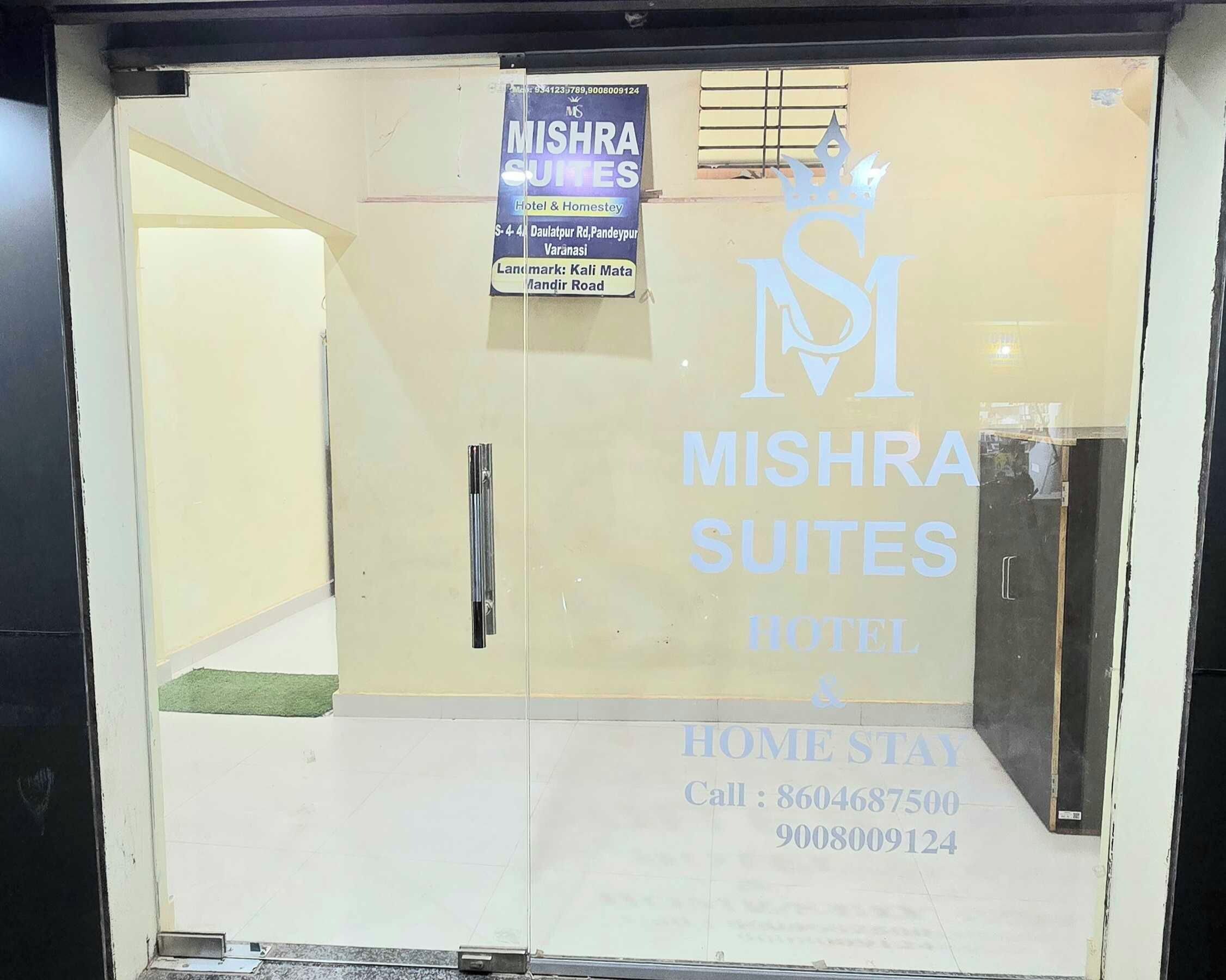 Entrada de un hotel con un letrero que indica Mishra Suites Hotel & Homestay, con números de contacto y dirección.