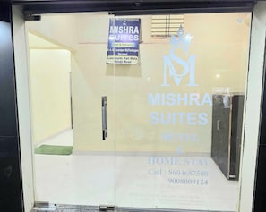 A hotel entrance with a sign for Mishra Suites Hotel & Homestay, including contact numbers and address. - Hotel O Mishra Suites (Varanasi)