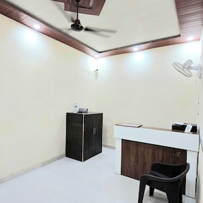 A room with a ceiling fan, a desk with a chair, and a cabinet. - Hotel O Mishra Suites (Varanasi)