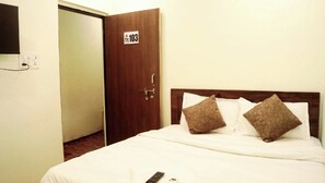A hotel room with a bed, two pillows, a remote control, and a door with a number sign. - Hotel O Mishra Suites (Varanasi)