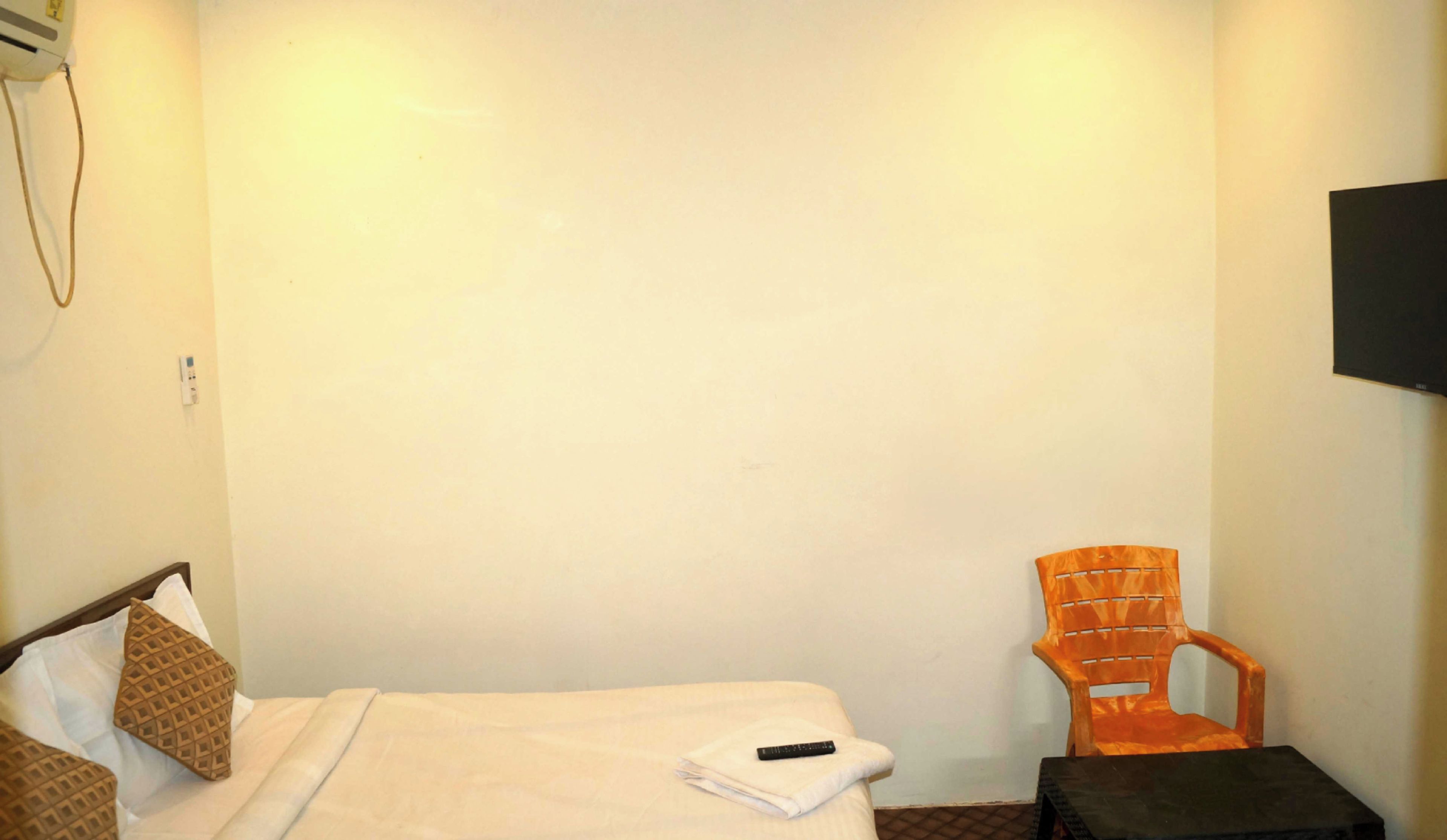 Una habitación pequeña y sencilla con una cama, una silla y un televisor montado en la pared.