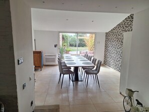 Un vaste espace de salle à manger avec une grande table et des chaises, une porte-fenêtre coulissante donnant sur un jardin et un mur décoré de motifs.