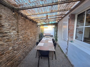 Un espace extérieur aménagé, abrité et doté de sièges, avec un mur en pierre d’un côté et une fenêtre de l’autre.