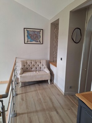 Una habitación con un sofá capitonado, un mapa en la pared y una puerta con pomo circular.