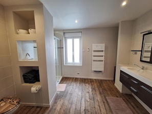 Une salle de bain moderne avec un plancher en bois, un grand miroir, un lavabo blanc et un porte-serviettes.