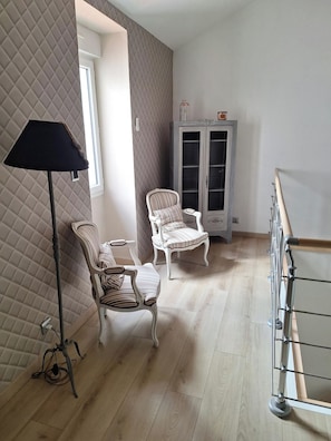 Una habitación con dos sillones tapizados, una lámpara de pie, un aparador con puertas de cristal y una barandilla de madera.
