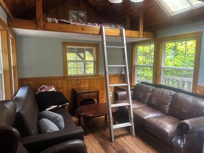Un salon chaleureux avec un plafond en bois, un canapé en cuir marron, une table en bois et une échelle.
