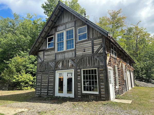 Une cabane en bois avec un toit à pignon, une porte d’entrée et plusieurs fenêtres.