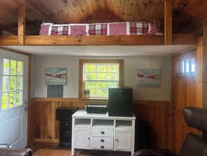 Une pièce avec un lit en mezzanine, une commode blanche, un haut-parleur noir et deux tableaux accrochés aux murs.
